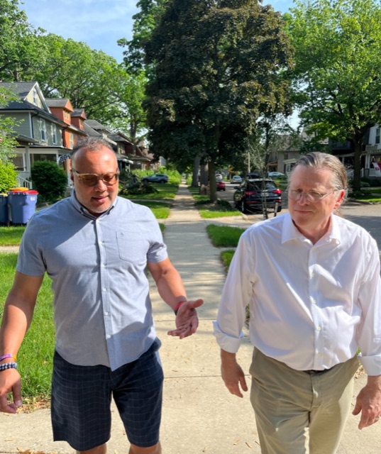 Dave Bulkowski walking and talking with a resident down a tree-lined Grand Rapids street.